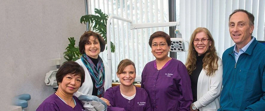 Dr. Sanker with members of the practice team in a treatment room, the team in matching purple scrubs.